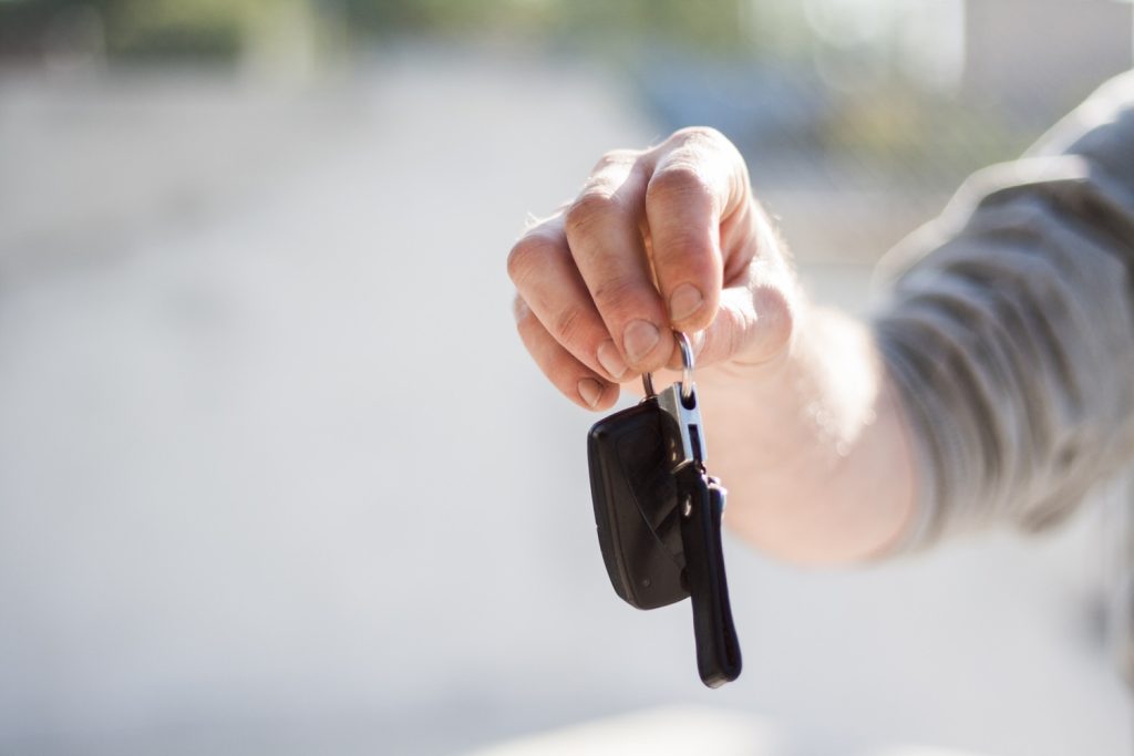 A close-up of a person's hand holding a set of car keys, with a key fob and a metal key hanging from a keyring.