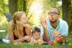 A happy family with a baby sitting on a picnic blanket in a sunny park, with the father blowing bubbles and the mother watching joyfully.